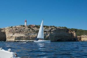 Beautiful coastal landscape seen from a boat. Cliffs, lighthouse and white yacht. Algarve, Portugal photo