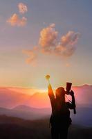 mujer viajera levanta la mano por su éxito con la puesta de sol en el fondo natural de las montañas. foto