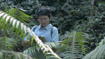 Woman botanist is researching plant species and working on digital tablet in tropical rainforest.