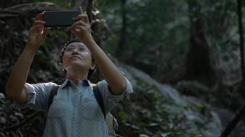 Woman traveler with backpack recording video from mobile smartphone in tropical rainforest.