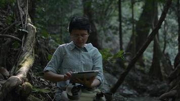 mujer asiática investigadora natural usando tableta digital en la selva tropical. video