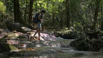 Female hiker with backpack walking over water stream among beautiful tropical forest.