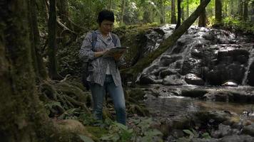 Female nature researcher working on digital tablet in tropical forest. video