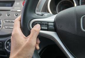 A hand pushes the cruise control button on a steering wheel. photo
