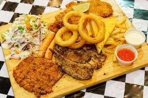 Mixed steak and french fries with dipping sauce on a wooden chopping board photo