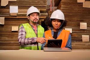 African American Female worker in a safety uniform and hard hat and male colleague inspect storage, stock order at factory warehouse, piles of stacking paper manufacture, industry product management.