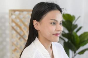 mujer feliz y hermosa con albornoz blanco aplicando crema hidratante en la cara, cuidado de la piel y concepto de tratamiento foto