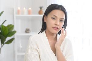 mujer feliz y hermosa con albornoz blanco aplicando crema hidratante en la cara, cuidado de la piel y concepto de tratamiento foto