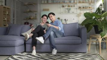 joven pareja gay sonriente usando smartphone y relajándose en la sala de estar en casa, lgbtq y concepto de diversidad. foto