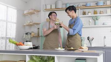 Young smiling gay couple making healthy juice with juice machine in the kitchen at home, LGBTQ and diversity concept. photo