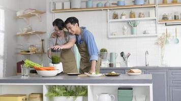 joven pareja gay sonriente haciendo jugo saludable con máquina de jugo en la cocina en casa, lgbtq y concepto de diversidad. foto