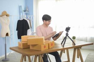 An Asian man is showing clothes in front of smartphone  live streaming at his shop. Technology online business concept. photo