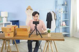 An Asian man is showing clothes in front of smartphone  live streaming at his shop. Technology online business concept. photo