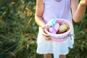 Cute funny girl with painted Easter eggs in spring in nature in a field with golden sunlight and flowers. Easter holiday, Easter bunny with ears, colorful eggs in a basket. Lifestyle photo