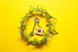 House key with keychain on yellow background and spring bouquet of branches with leaves. Farmhouse, tourism accommodation, booking, moving to new home, mortgage, rent and buy real estate, summer offer photo