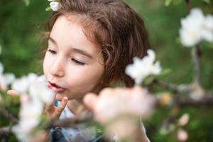 A cute little girl of 5 years old in a blooming white apple orchard in spring. Springtime, orchard, flowering, allergy, spring fragrance, tenderness, caring for nature. Portrait photo