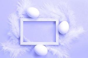 Easter white frame on purple background very peri tinting of chicken eggs and colored delicate feathers. Spring, religious holiday, Easter decoration, greeting, copy space, mock up photo