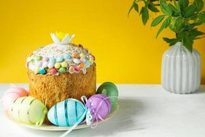 Easter cake with painted eggs on a platter in a white table. Traditional festive food. Yellow background photo