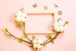Frame made of cotton flowers, delicate little leaves from open buds on branches-sprouts on a pink background and carved wood butterflies, birds, ornaments. Spring, new life, tenderness. Copy space