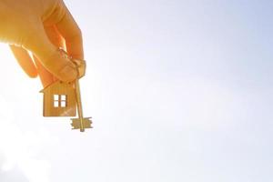 Wooden pendant of a house and key. Background of the sky and field. Dream of home, building a cottage in the countryside, plan and design, delivery of the project, moving to a new house. Copy space photo