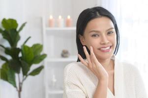 mujer feliz y hermosa con albornoz blanco aplicando crema hidratante en la cara, cuidado de la piel y concepto de tratamiento foto