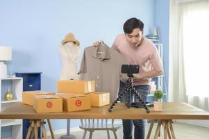 An Asian man is showing clothes in front of smartphone  live streaming at his shop. Technology online business concept. photo