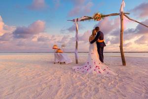 la novia y el novio bajo el arco de la boda en la playa. fondo de boda romántica. increíble puesta de sol en la playa, vista infinita al mar, cielo romántico con nubes. destino idílico luna de miel foto