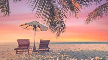 Beautiful tropical sunset scenery, two sun beds, loungers, umbrella under palm tree. White sand, sea view with horizon, colorful twilight sky, calmness and relaxation. Inspirational beach resort hotel photo