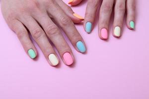 Colored matte manicure on female hands on a pink background with copy space photo