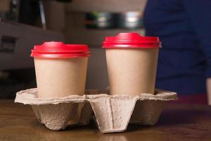 Mock-up two cardboard cups with coffee in a takeaway stand in the interior of small cafe.. Coffee to go concept photo