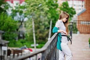 Trendy girl at glasses and ripped jeans against barrier on street. photo