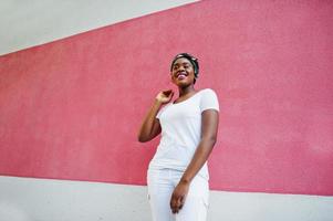 retrato de una elegante chica afroamericana, vestida con ropa blanca, contra una pared rosa. moda callejera de jóvenes negros. foto