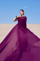 Amazing beautiful brunette woman with the Peacock feather in purple fabric in the desert. Oriental, Indian, fashion, style concept photo