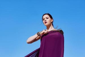 Amazing beautiful brunette woman with the Peacock feather in purple fabric in the desert. Oriental, Indian, fashion, style concept photo