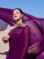 Amazing beautiful brunette woman with the Peacock feather in purple fabric in the desert. Oriental, Indian, fashion, style concept photo