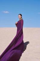 Amazing beautiful brunette woman with the Peacock feather in purple fabric in the desert. Oriental, Indian, fashion, style concept photo
