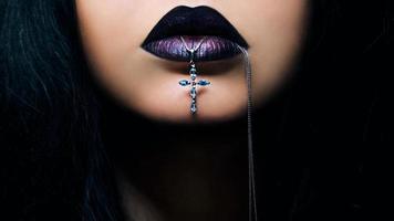 Portrait of dark hair woman with dark lips with cross in her mouth photo