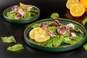 Fresh salad with pickled octopus, beet leaves and lemon, dark background photo