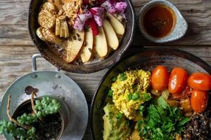 Top View Food Photo of Healthy Vegan Meal with Scrambled Tofu, Cherry, Tomatoes, Avocado, Black Beans and Porridge with Fresh Fruits