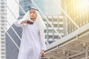 Portrait of Smiling Arab Middle Eastern Businessman checking time and using smartphone in the city background photo