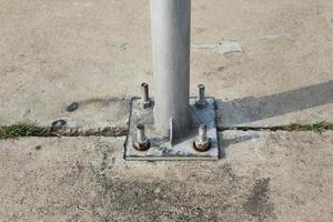 Welded pole to base plate and connecting them to footing with anchor bolts. Studs with heavy hex nut. Carbon steel plate and column on the concrete floor. photo