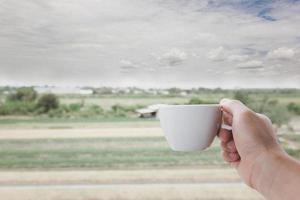 A white man's hand holding a hot coffee cup on the landscape field nature background. photo