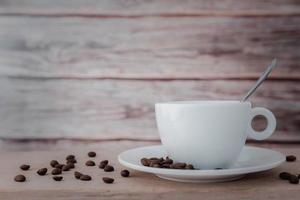 A white coffee cup and coffee beans with a spoon in the cup and a saucer is placed on a wooden plate and on a wooden background. photo