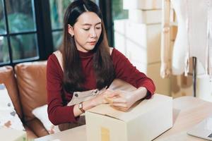 SME small business woman packing and taping carton box. entrepreneur or shop owner working at home. Preparing for delivery, online e-commerce photo