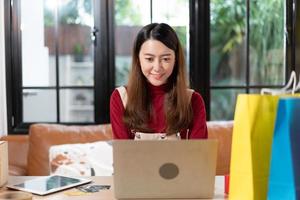 PYME empresaria asiática de pequeñas empresas o propietaria de una tienda que usa una computadora portátil para verificar el pedido de existencias. mujer que trabaja para la tienda en línea en casa. gestión nuevo estilo de vida normal foto