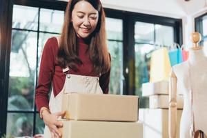 SME small business Asian female entrepreneur or shop owner holding boxes preparing customer order before shipping delivery. drop shipping commerce retail, startup business, freelancer working at home photo