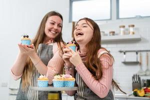 Little girl laughing and holding homemade cupcake with mother in the kitchen at home. Family time enjoy baking bakery together. photo
