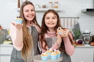 Happy mother and daughter showing smiling and showing homemade cake or cupcakes looking at camera in the kitchen. family activity baking bakery at home on weekend photo