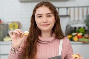 Caucasian girl in apron proud showing homemade cookies to camera. happy kid baking bakery in the kitchen on weekend. photo