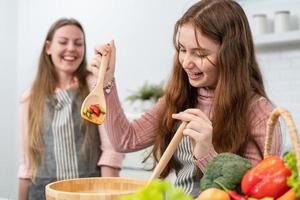 Happy mother watching daughter learn to cooking homemade salad in the kitchen. family activity on weekend. preparing food for lunch. parent support kid to improve skill photo